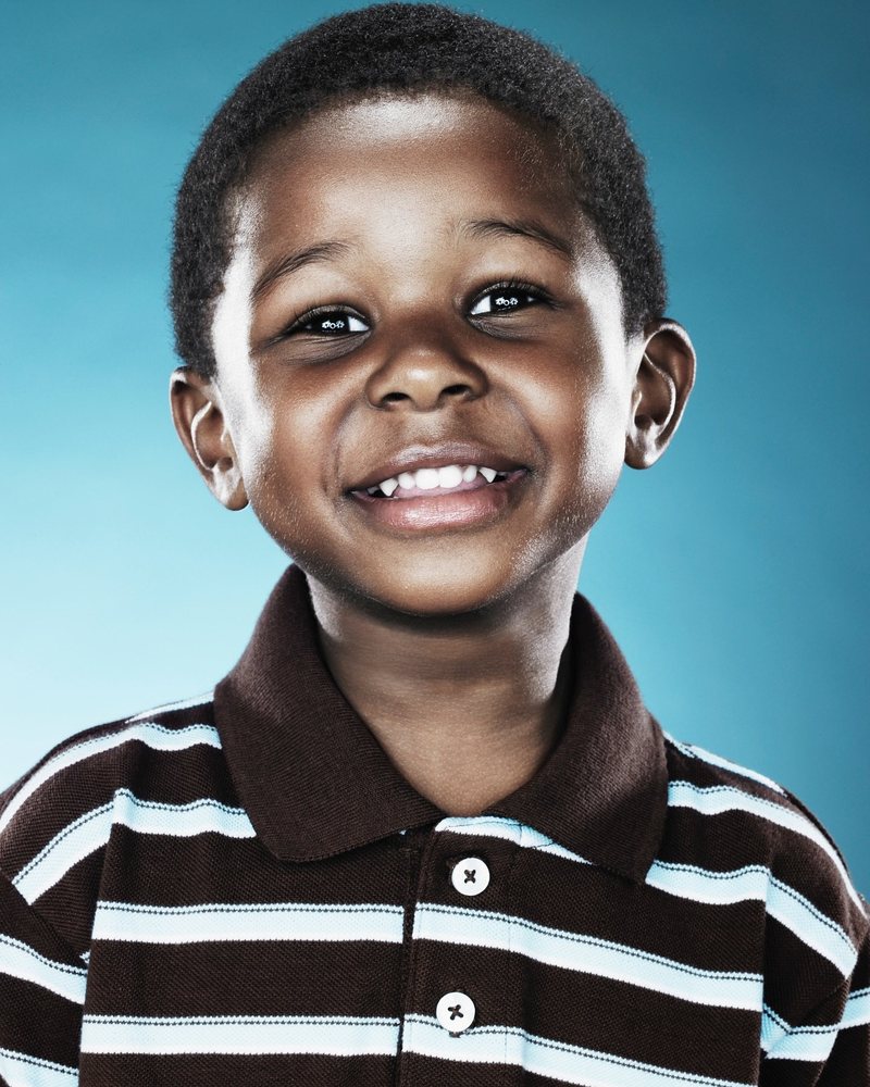 Boy in a striped polo laughing on a blue backdrop