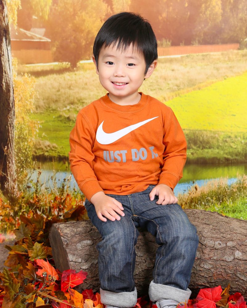 Boy in an orange shirt sitting on a log among autumn leaves